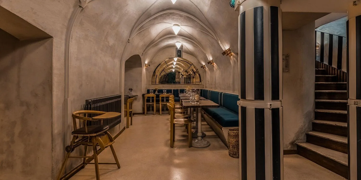 Le caveau voûté au sous-sol, banquette verte et tables en bois